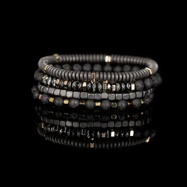 Men’s layered bracelet set featuring matte black lava stone beads, gray heishi beads, silver-tone hematite cube beads, faceted hematite crystal beads, and gold-tone spacer accents, stacked in a sophisticated industrial luxury design on a white background.
