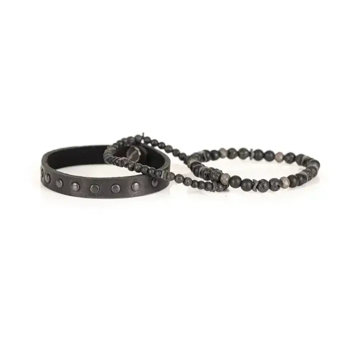 Black multi-layer men’s bracelet set featuring studded leather band, matte onyx beads, lava stone, faceted hematite accents, and layered black beaded strands on a light background.