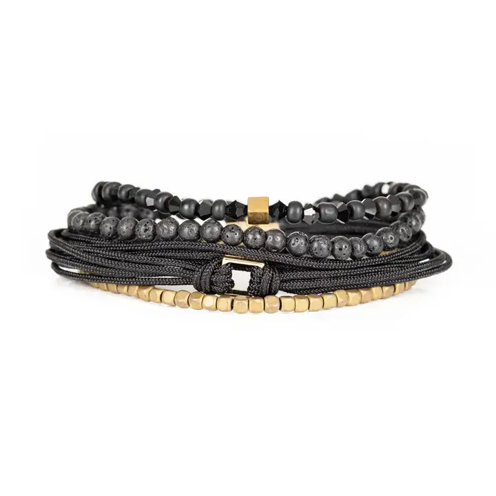 Black and gold layered men’s bracelet set with lava stone beads, gold cube accents, faceted black beads, braided rope wraps, and metallic centerpiece on white background.