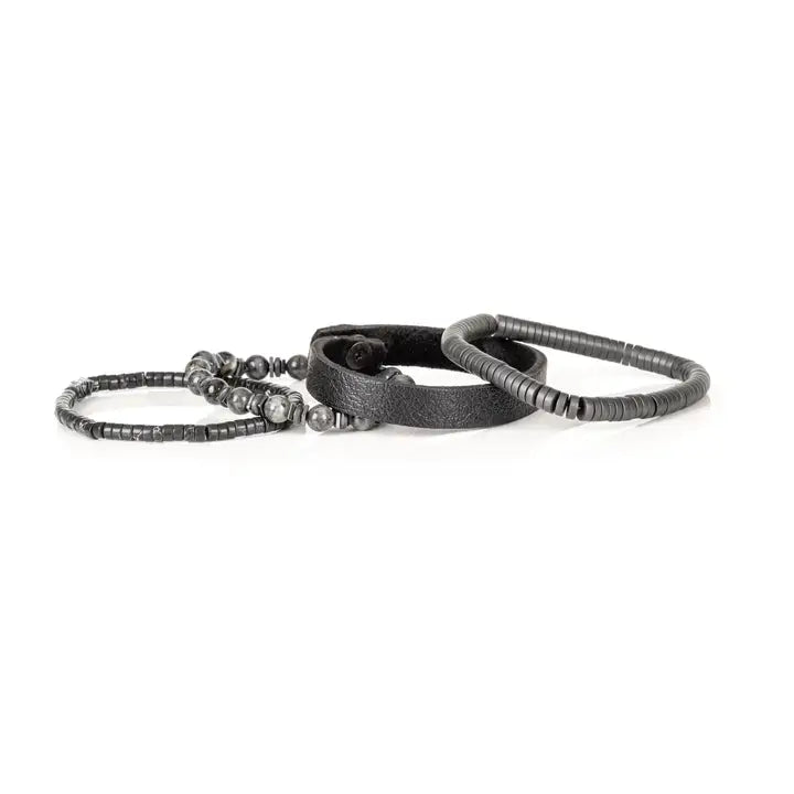 Black multi-layer men’s bracelet featuring textured leather band, gunmetal hematite bead strands, matte grey stone beads, and layered metallic accents on a light background.