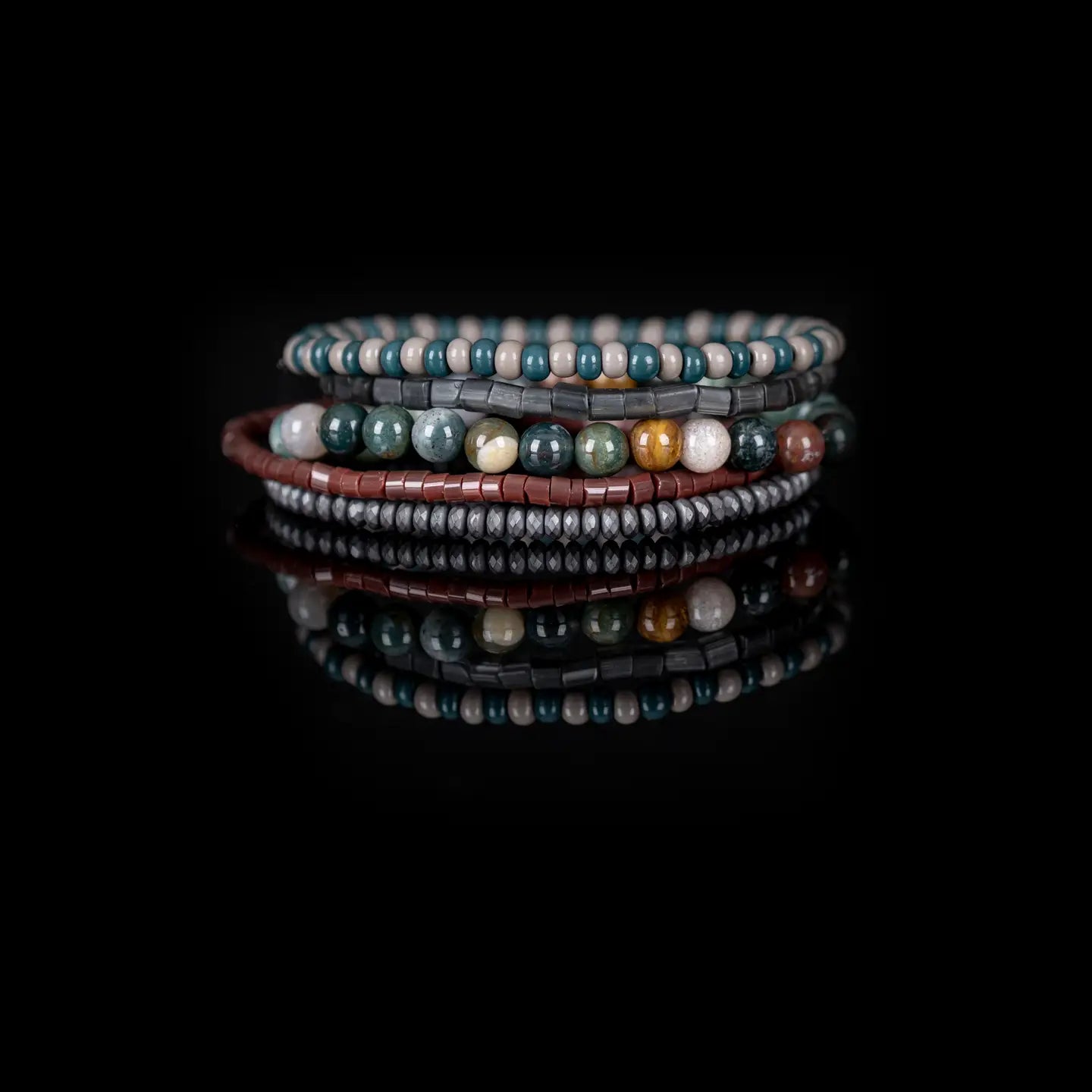 Men’s layered bracelet set featuring teal and beige bead strands, smoky gray translucent beads, multicolor natural stone beads in green, cream, and earth tones, reddish-brown heishi beads, and faceted hematite spacer beads, stacked in a sophisticated earthy luxury design on a white background.