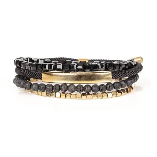 Men’s layered bracelet set featuring faceted black crystal beads, matte black lava stone beads, black braided cord, a polished gold-tone bar centerpiece, and gold-tone hematite-style spacer beads, stacked in a sophisticated black and gold luxury design on a white background.