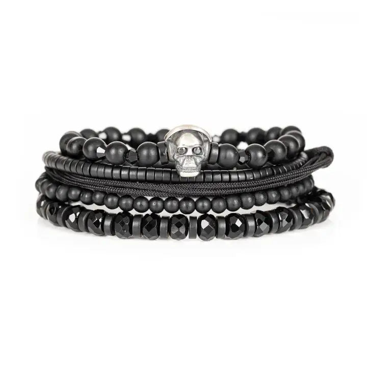 Black layered men’s bracelet set with matte black beads, silver skull centerpiece, faceted crystal accents, and braided rope wraps on white background.