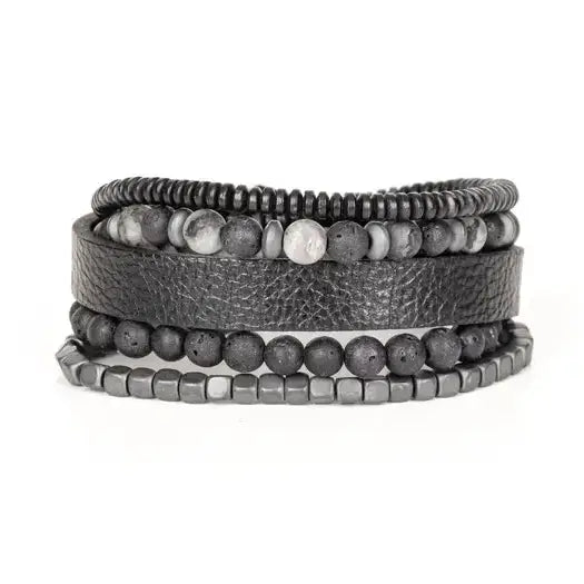 Men’s layered bracelet set featuring a black textured leather cuff, matte black lava stone beads, gray marbled stone beads, hematite cube beads, and black heishi spacers, stacked in a rugged contemporary luxury design on a white background.