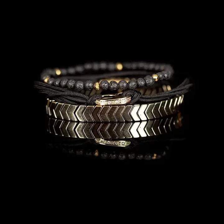 Black and gold layered men’s bracelet with lava stone beads, braided rope wraps, gold chevron metal bar, and metallic accents on white background.