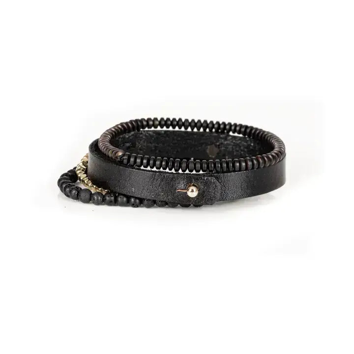 Men’s layered bracelet set featuring a black leather cuff with a polished gold-tone ID plate, matte black lava stone beads, gold-tone hematite spacer beads, and black heishi beads, stacked in a sophisticated black and gold luxury design on a white background.