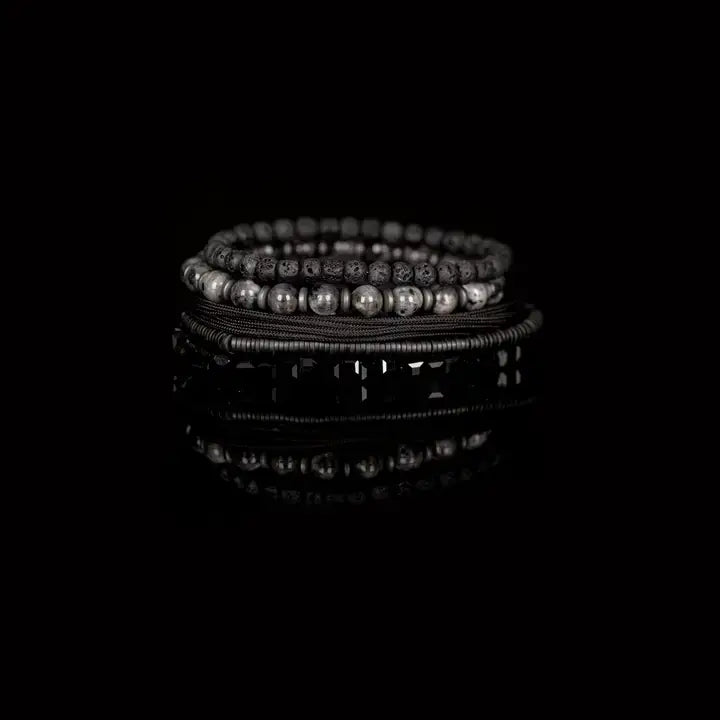 Men’s layered bracelet set featuring black faceted crystal beads, matte black lava stone beads, black braided cord, hematite spacer beads, and polished gray stone beads, stacked in a bold monochromatic luxury design on a white background.