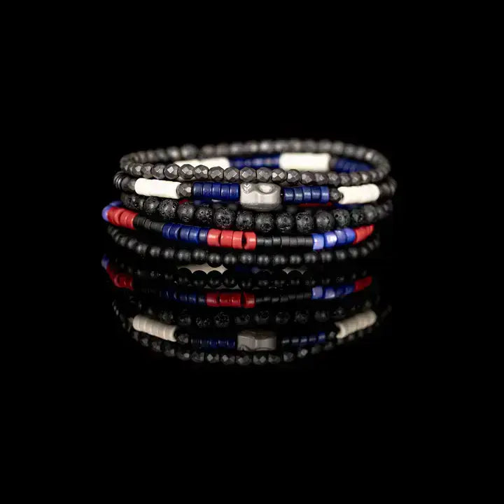 Black multi-layer men’s bracelet featuring lava stone beads, faceted hematite beads, blue cylindrical accents, red and white spacer details, and layered black bead strands on a light background.