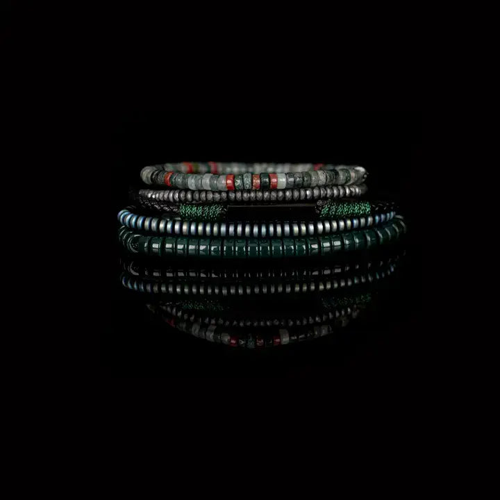 Men’s layered bracelet set featuring dark green heishi beads, green woven cord, black braided leather, hematite spacer beads, and green-gray natural stone beads with subtle red accents, stacked in a sophisticated earthy luxury design on a white background.