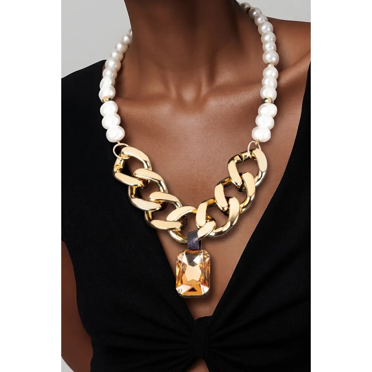 Gold chunky chain necklace with pearl detail and amber crystal pendant on white background.