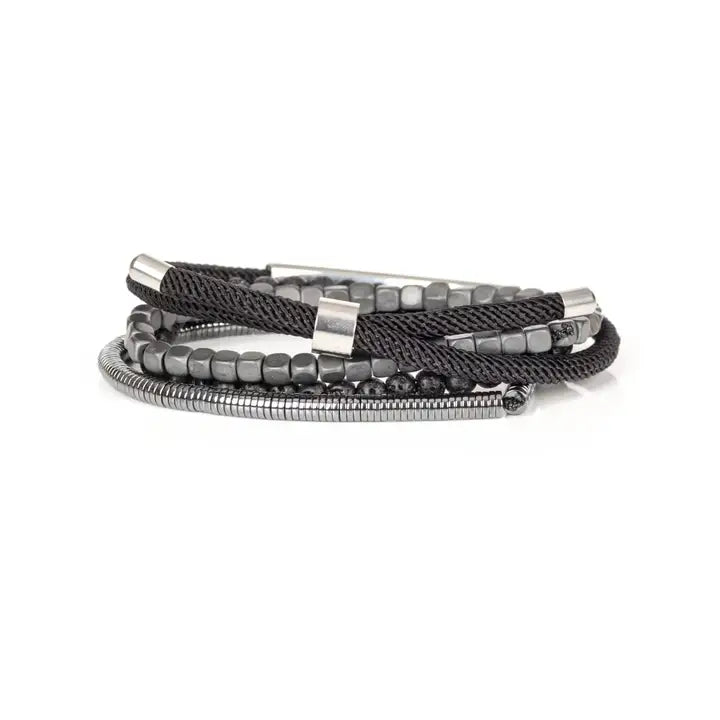 Men’s layered bracelet set featuring a polished silver-tone ID bar centerpiece, matte black lava stone beads, gunmetal cube beads, black braided cord wraps, and silver-tone coil wrap accents, stacked in a sleek industrial luxury design on a white background.