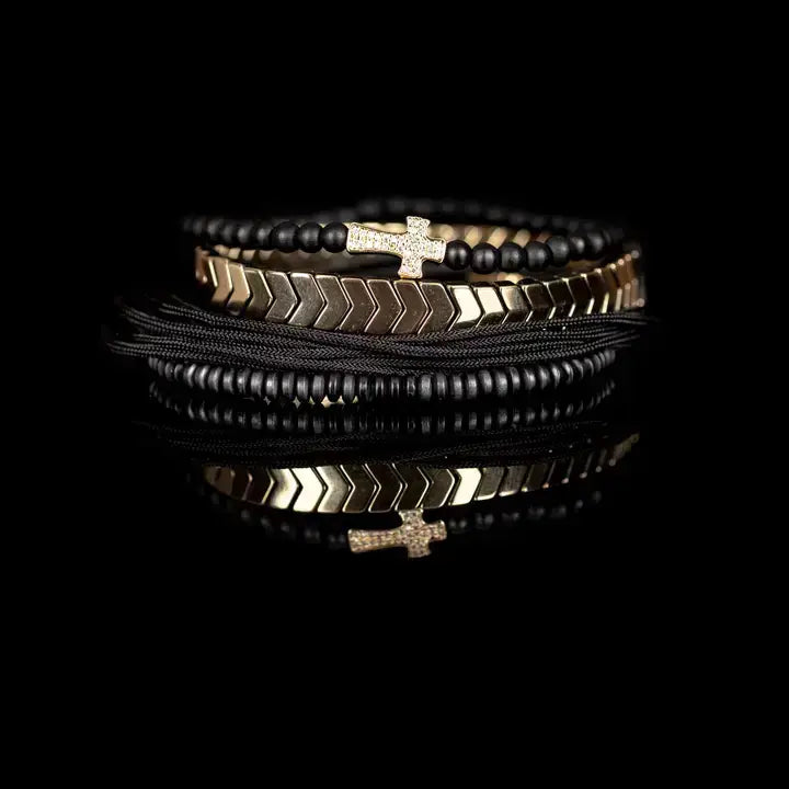 Black multi-layer men’s bracelet set with matte black beads, gold chevron metal bar, black cords, and cross accent detail on white background.