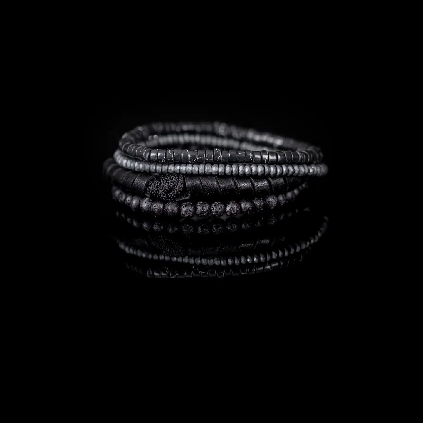 Men’s layered bracelet set featuring matte black lava stone beads, black leather-wrapped cord, black marbled heishi beads, faceted gray crystal beads, and dark metallic spacer beads, stacked in a sleek monochromatic luxury design on a white background.