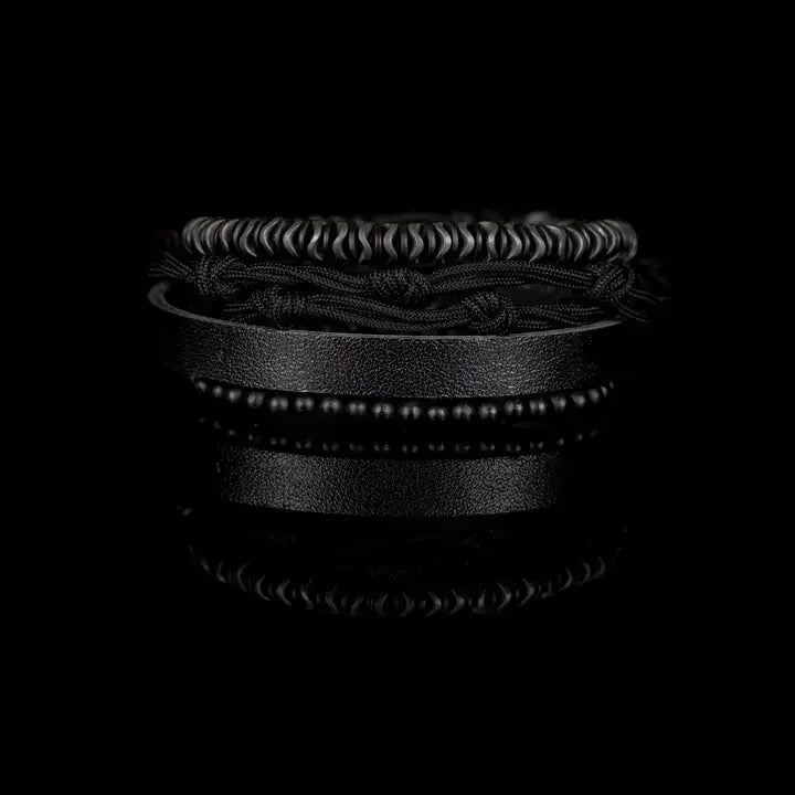 Black multi-layer men’s bracelet featuring hematite disc beads, braided black rope layers, smooth black leather band, and matte black bead strand on a light background.