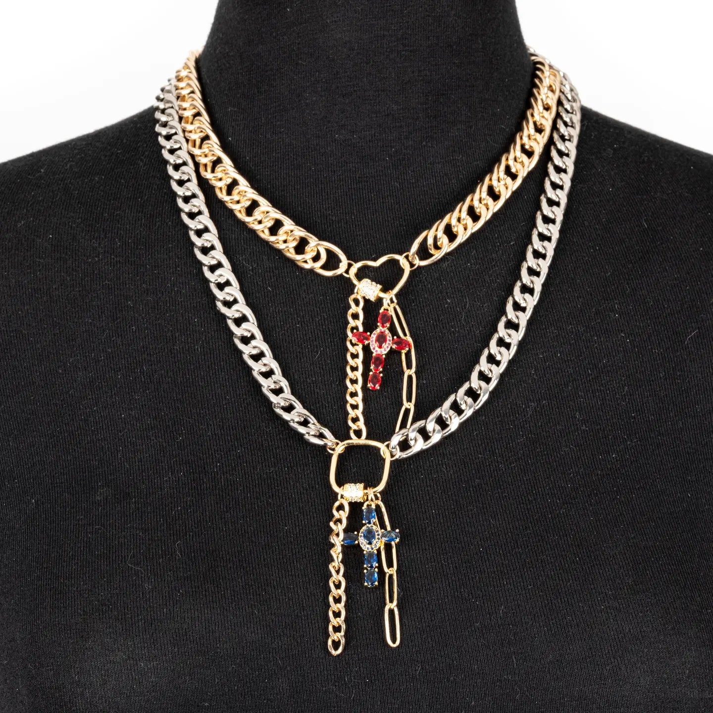 Mixed metal chain necklace with red and blue cross charms and layered drop chains on white background.