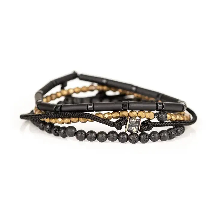 Black and gold multi-layer men’s bracelet featuring matte black tubular beads, faceted gold hematite strands, braided black cord, lava stone beads, and crystal accent detail on a light background.