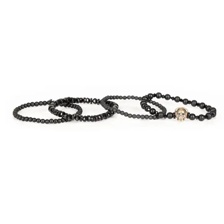 Black layered men’s bracelet set with matte black beads, gold skull centerpiece, faceted crystal accents, and geometric spacer beads on white background.