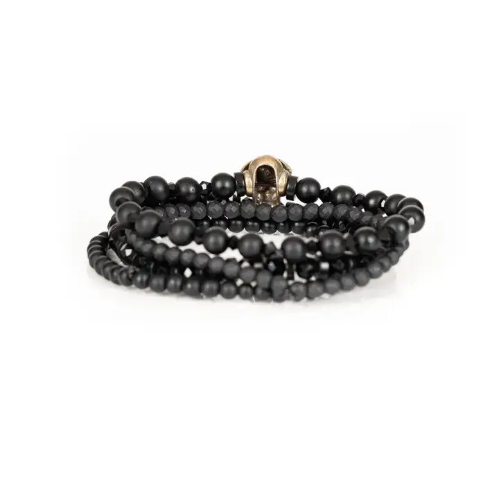 Black layered men’s bracelet set with matte black beads, gold skull centerpiece, faceted crystal accents, and geometric spacer beads on white background.