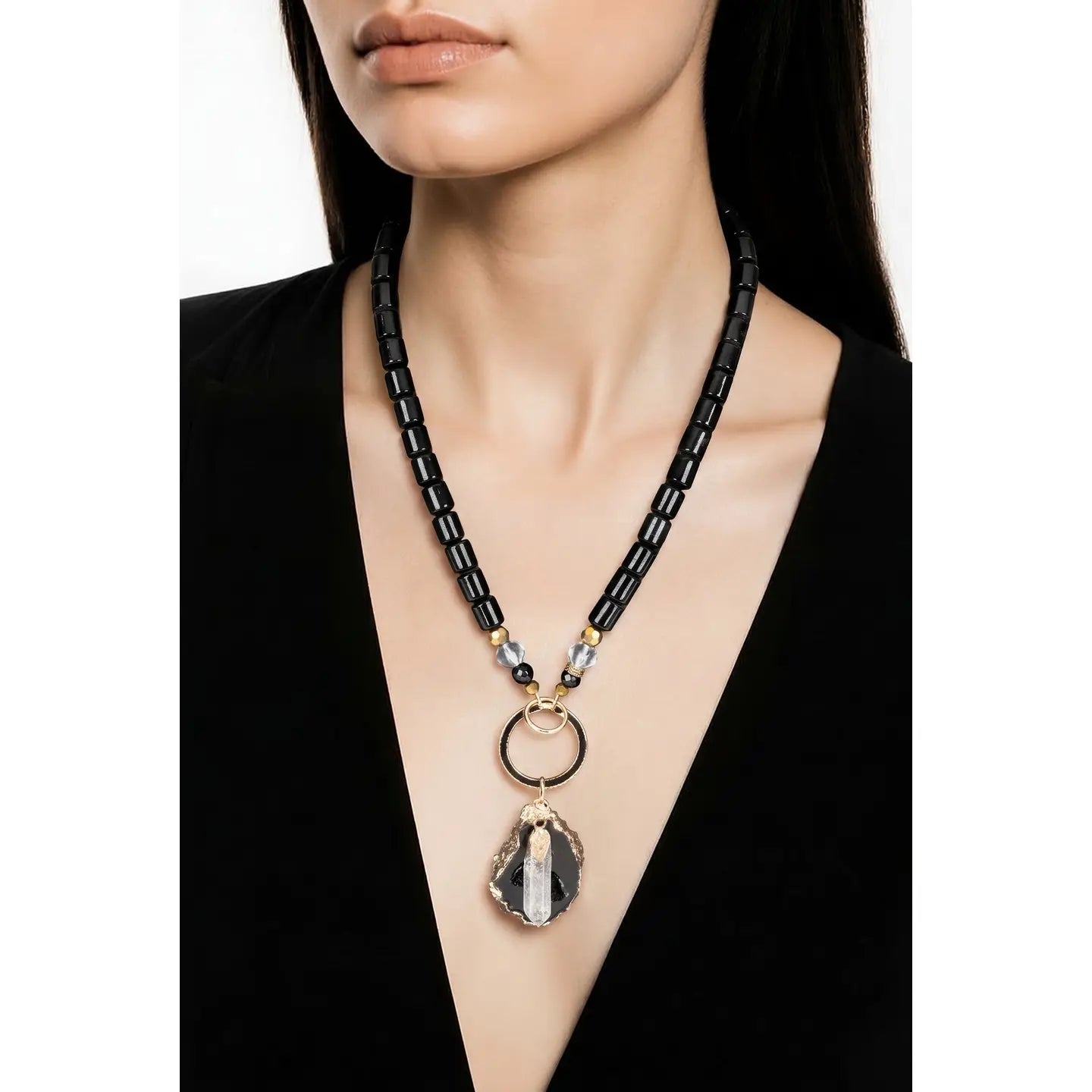 Black beaded necklace with gold ring connector and raw stone crystal pendant on white background.