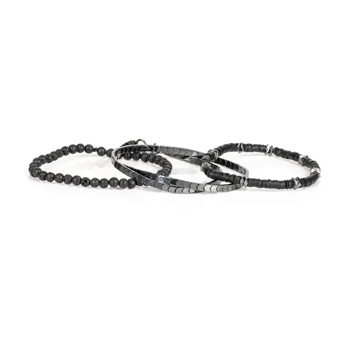 Black multi-layer men’s bracelet featuring hematite disc strands, shield-pattern metallic beads, pyramid-cut spacers, and lava stone bead accents on a light background.