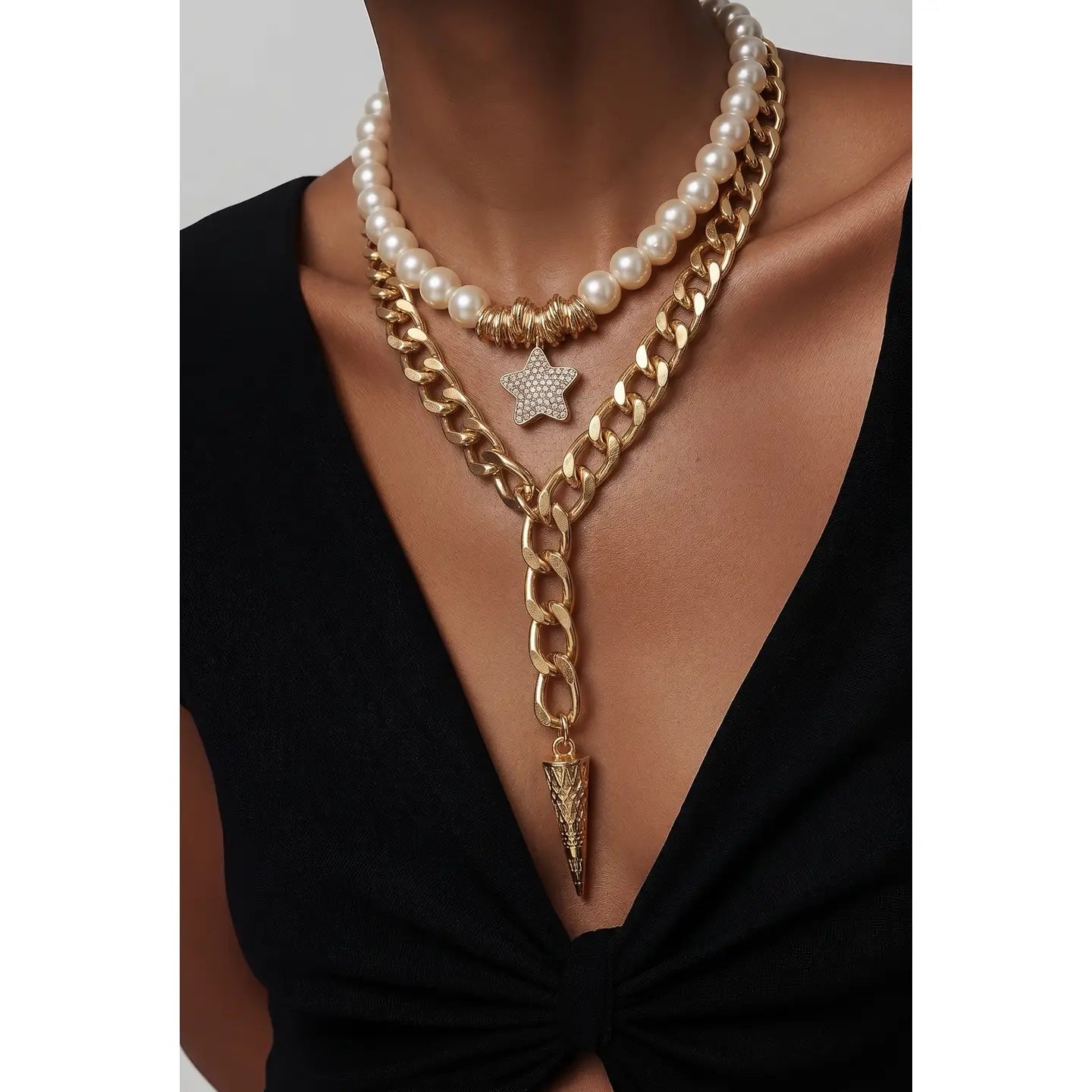 Layered necklace with white pearls, gold chain, star charm, and a spike pendant drop, displayed on a white background.