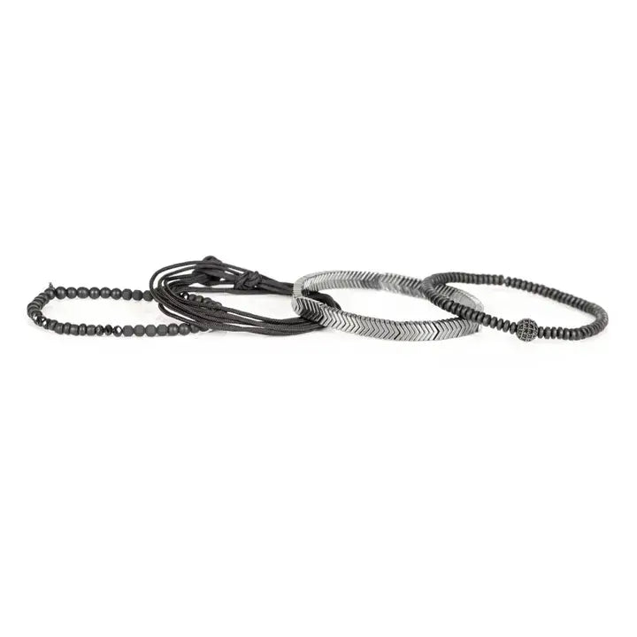 Black multi-layer men’s bracelet featuring silver chevron metal bar, hematite bead strands, crystal accent bead, faceted black stones, and braided black rope layers on a light background.