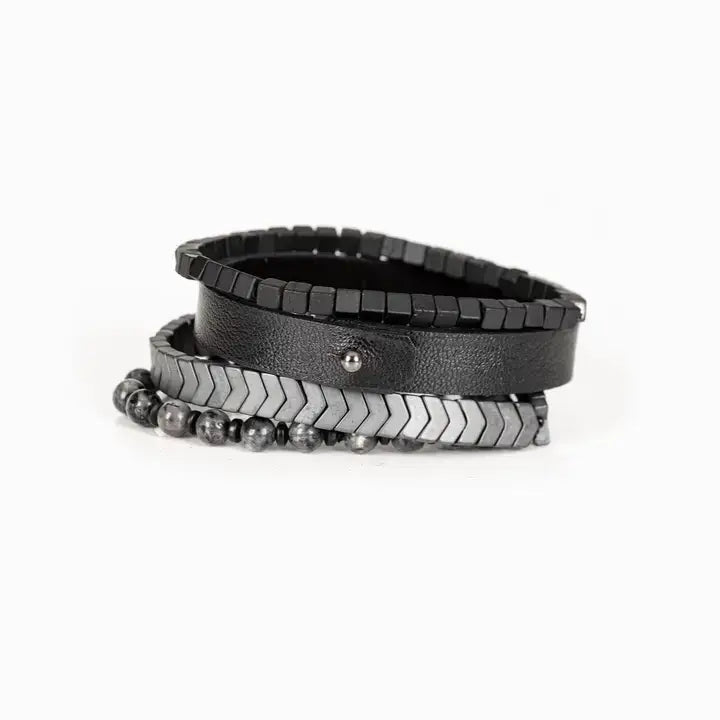 Men’s layered bracelet set featuring a black textured leather cuff, gunmetal cube bead bracelet, gunmetal chevron metal beads, and gray marbled natural stone beads, stacked in a bold industrial luxury design on a white background.
