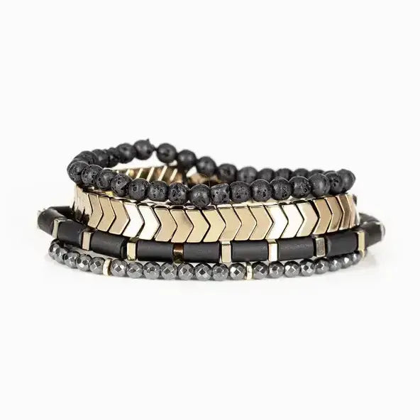 Men’s layered bracelet set featuring matte black lava stone beads, gold-tone chevron metal beads, black cylindrical beads with gold spacers, and faceted hematite beads, stacked in a modern luxury design on a white background.