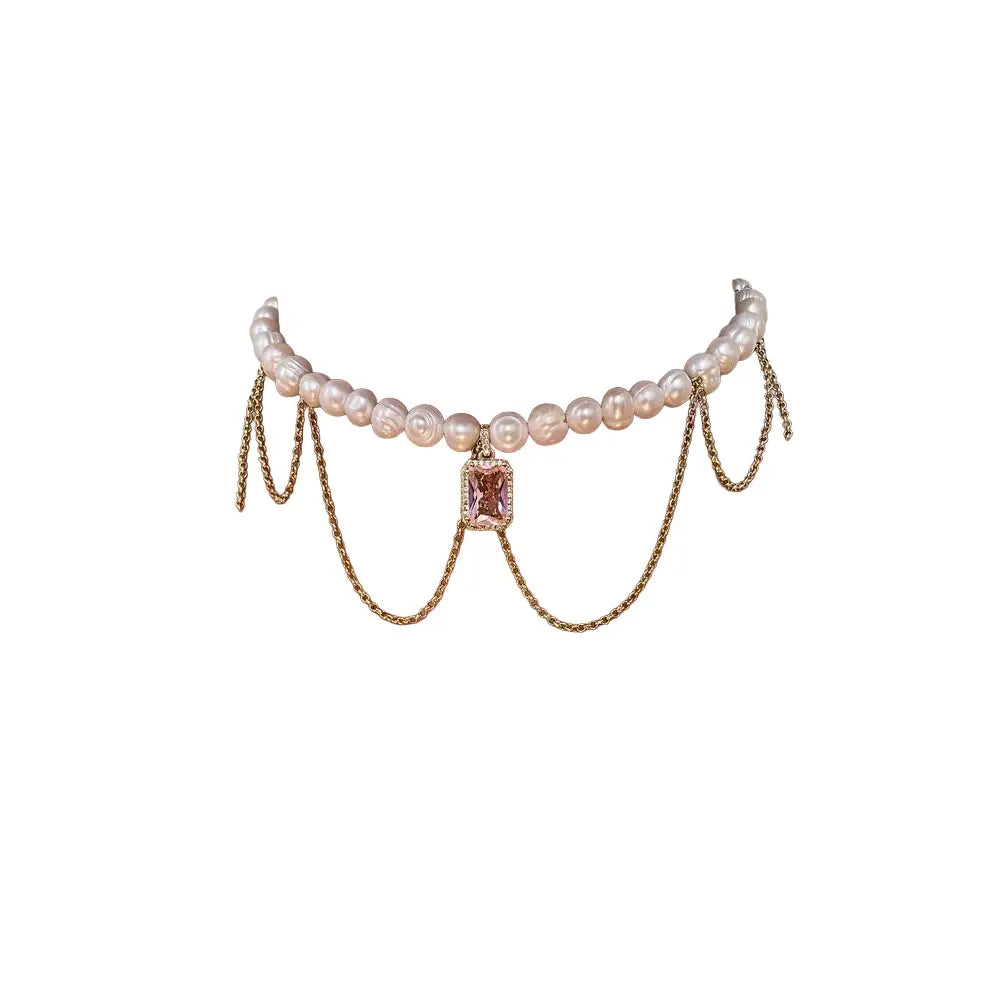 Pearl necklace with draped gold chains and a pink crystal pendant on a white background.