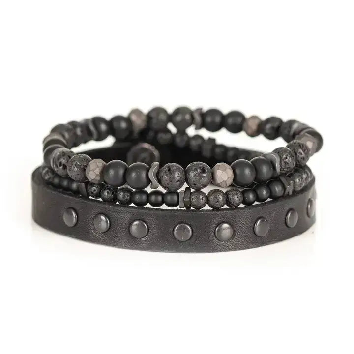 Black multi-layer men’s bracelet set featuring studded leather band, matte onyx beads, lava stone, faceted hematite accents, and layered black beaded strands on a light background.