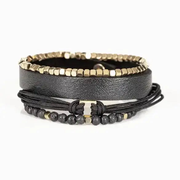 Men’s layered bracelet set featuring a black textured leather cuff, gold-tone faceted metal bead bracelet, black braided cord wrap, matte black lava stone beads, and gold-tone accent beads, stacked in a refined modern luxury design on a white background.