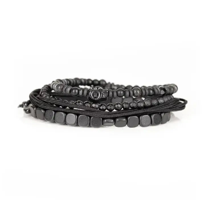 Black layered men’s bracelet set with hematite-style cube beads, matte black beads, faceted crystal accents, metallic centerpiece, and braided rope wraps on white background.