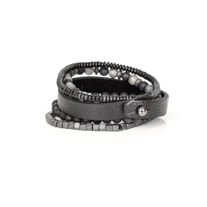 Men’s layered bracelet set featuring a black textured leather cuff, matte black lava stone beads, gray marbled stone beads, hematite cube beads, and black heishi spacers, stacked in a rugged contemporary luxury design on a white background.