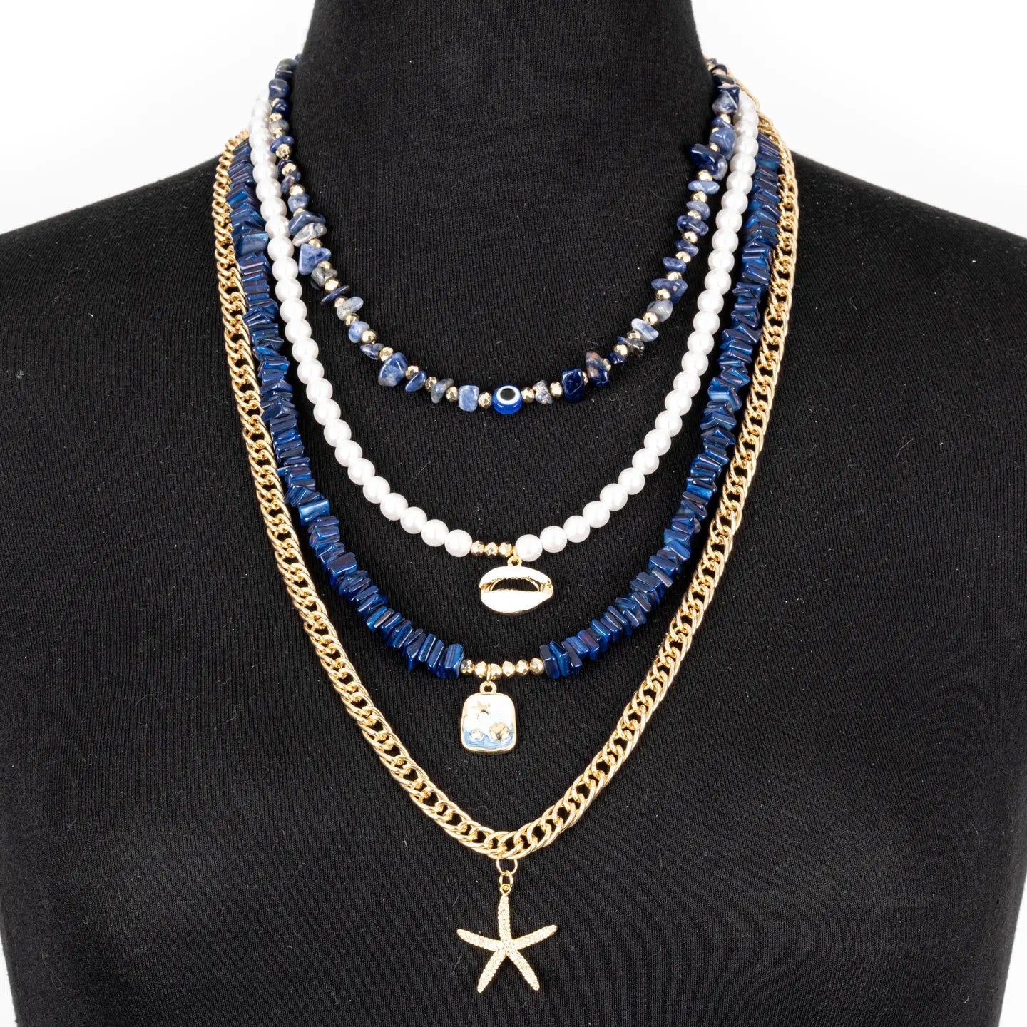 Layered blue and white bead necklace with gold chain and starfish pendant on white background.