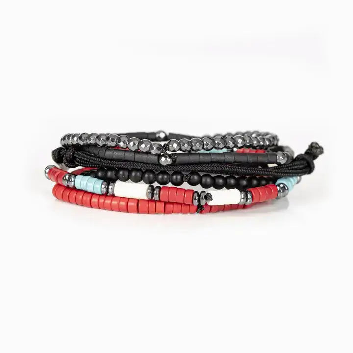 Men’s layered bracelet set featuring faceted hematite crystal beads, black heishi beads, turquoise and coral-red accent beads, matte black bead strands, black braided cord wraps, and a pavé-style gunmetal centerpiece, stacked in a bold contemporary bohemian luxury design on a white background.