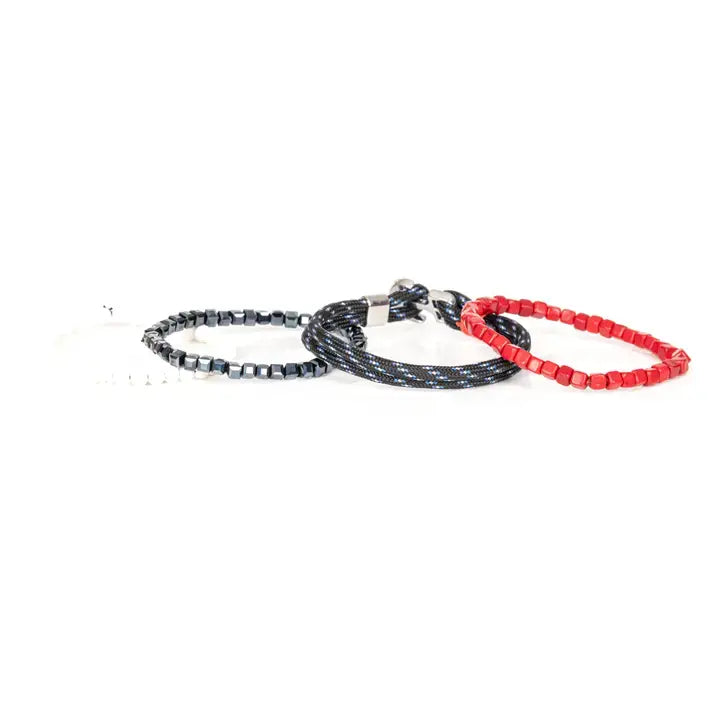 Men’s layered bracelet set featuring vibrant red cube beads, black braided cord with blue accents, faceted black hematite beads, and white heishi beads, stacked in a bold contemporary luxury design on a white background.