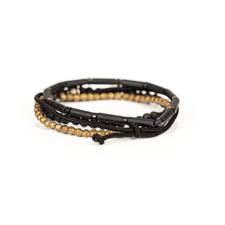 Black and gold multi-layer men’s bracelet featuring matte black tubular beads, faceted gold hematite strands, braided black cord, lava stone beads, and crystal accent detail on a light background.