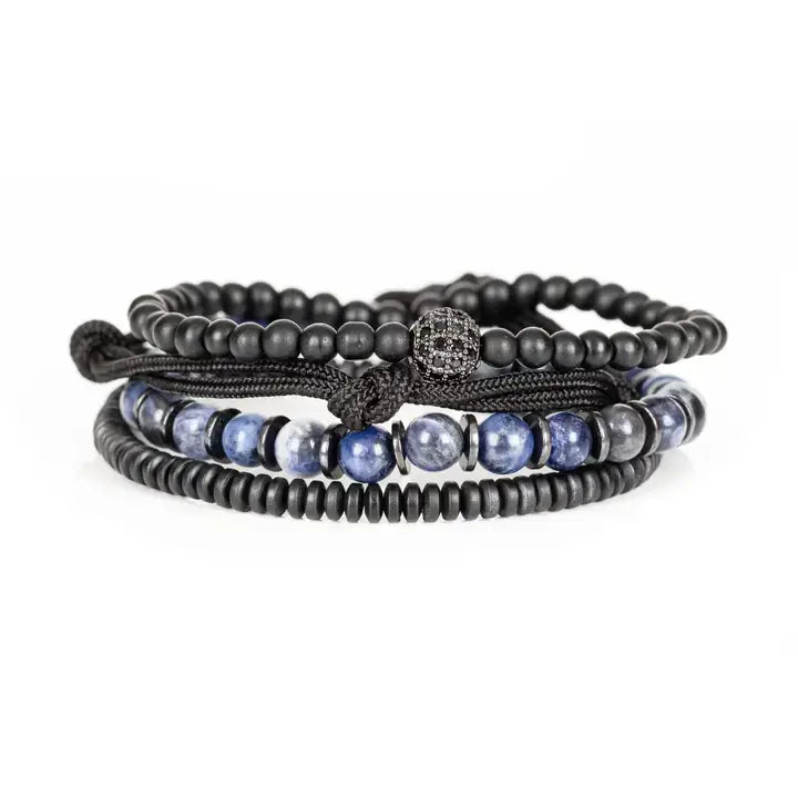 Black and blue layered men’s bracelet set with matte black beads, blue marbled stone accents, braided rope wraps, and pavé centerpiece on white background.