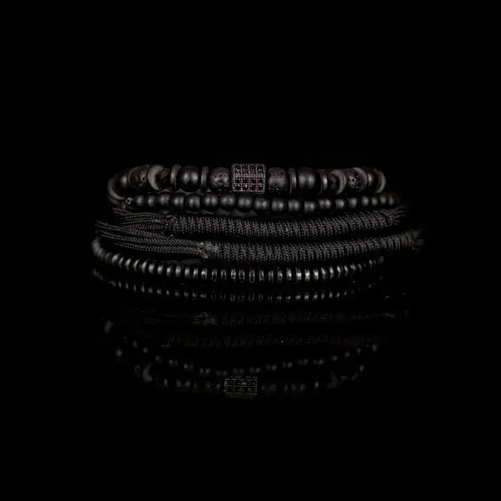 Black layered men’s bracelet set with matte black beads, lava stone accents, braided rope wraps, and dark pavé square detail on white background.