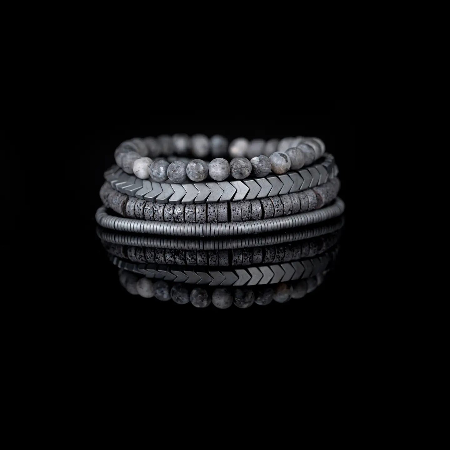 Men’s layered bracelet set featuring gray natural stone beads, gunmetal chevron metal beads, dark lava stone disc beads, and silver-tone coil wrap accents, stacked in a sleek monochromatic industrial luxury design on a white background.