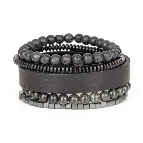Men’s layered bracelet set featuring a black leather cuff, matte black lava stone beads, dark gray natural stone beads, black heishi spacers, faceted black crystal beads, and hematite cube beads, stacked in a sophisticated monochromatic luxury design on a white background.