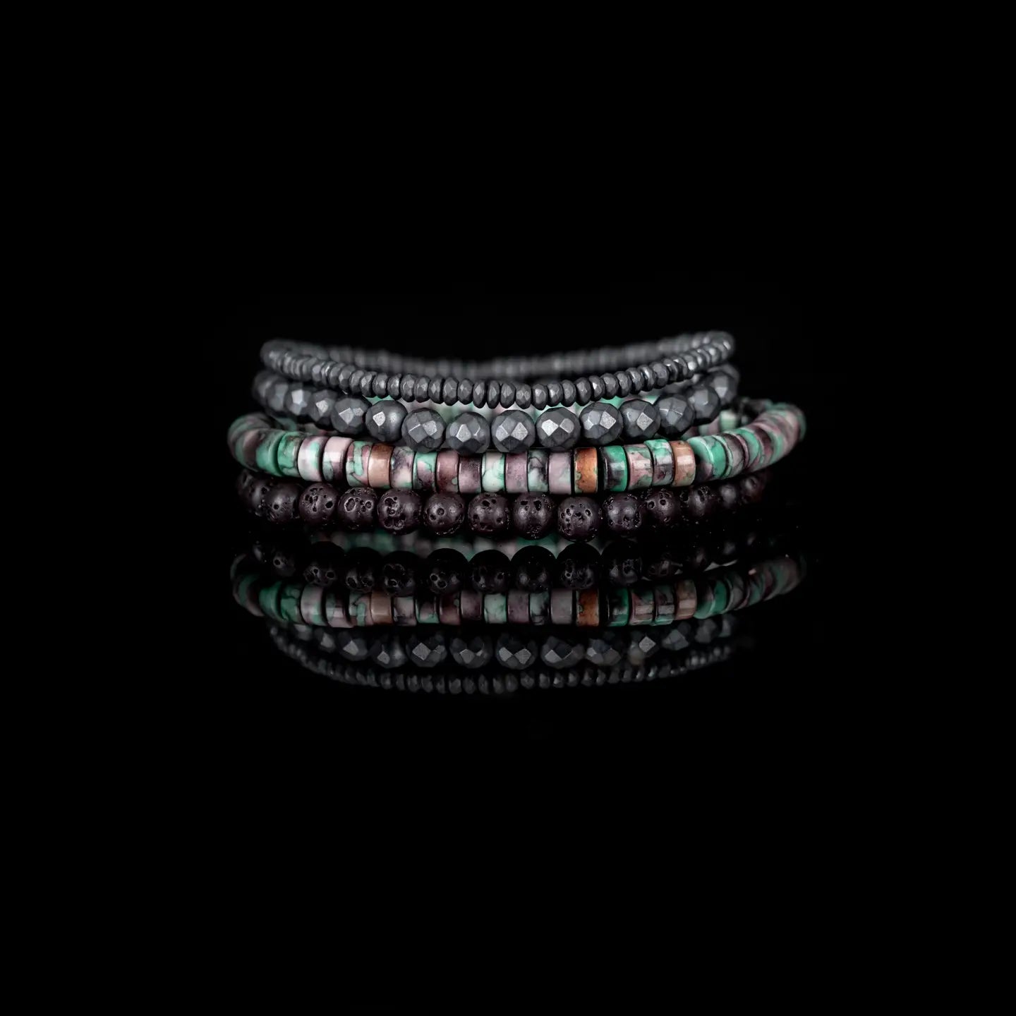 Men's layered bracelet set featuring faceted hematite beads, matte black lava stone beads, and natural heishi stone beads in turquoise, cream, mauve, and earthy brown tones arranged in a stacked design on a white background.