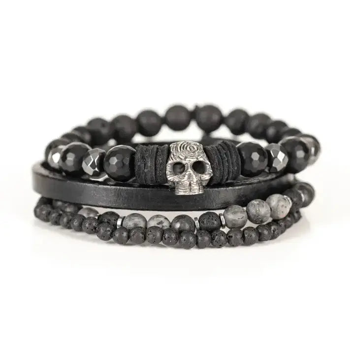 Black multi-layer men’s bracelet set featuring faceted black onyx beads, lava stone accents, black leather band, and silver skull centerpiece on a light background.