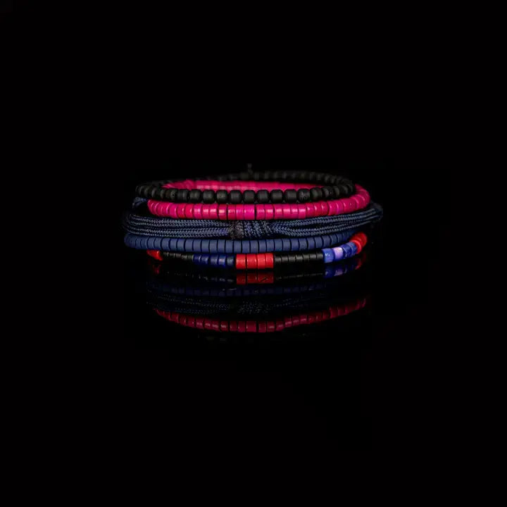 Men’s layered bracelet set featuring navy blue braided cord, blue, black, red, and fuchsia heishi beads, black cube beads, and marbled blue accent beads, stacked in a vibrant contemporary luxury design on a white background.