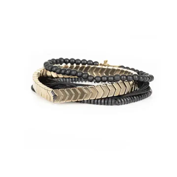 Black multi-layer men’s bracelet set with matte black beads, gold chevron metal bar, black cords, and cross accent detail on white background.