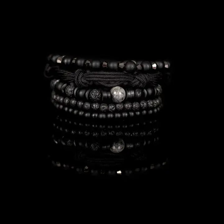 Black layered men’s bracelet set with matte black beads, lava stone accents, marbled centerpiece stone, faceted metallic beads, and braided rope wraps on white background.