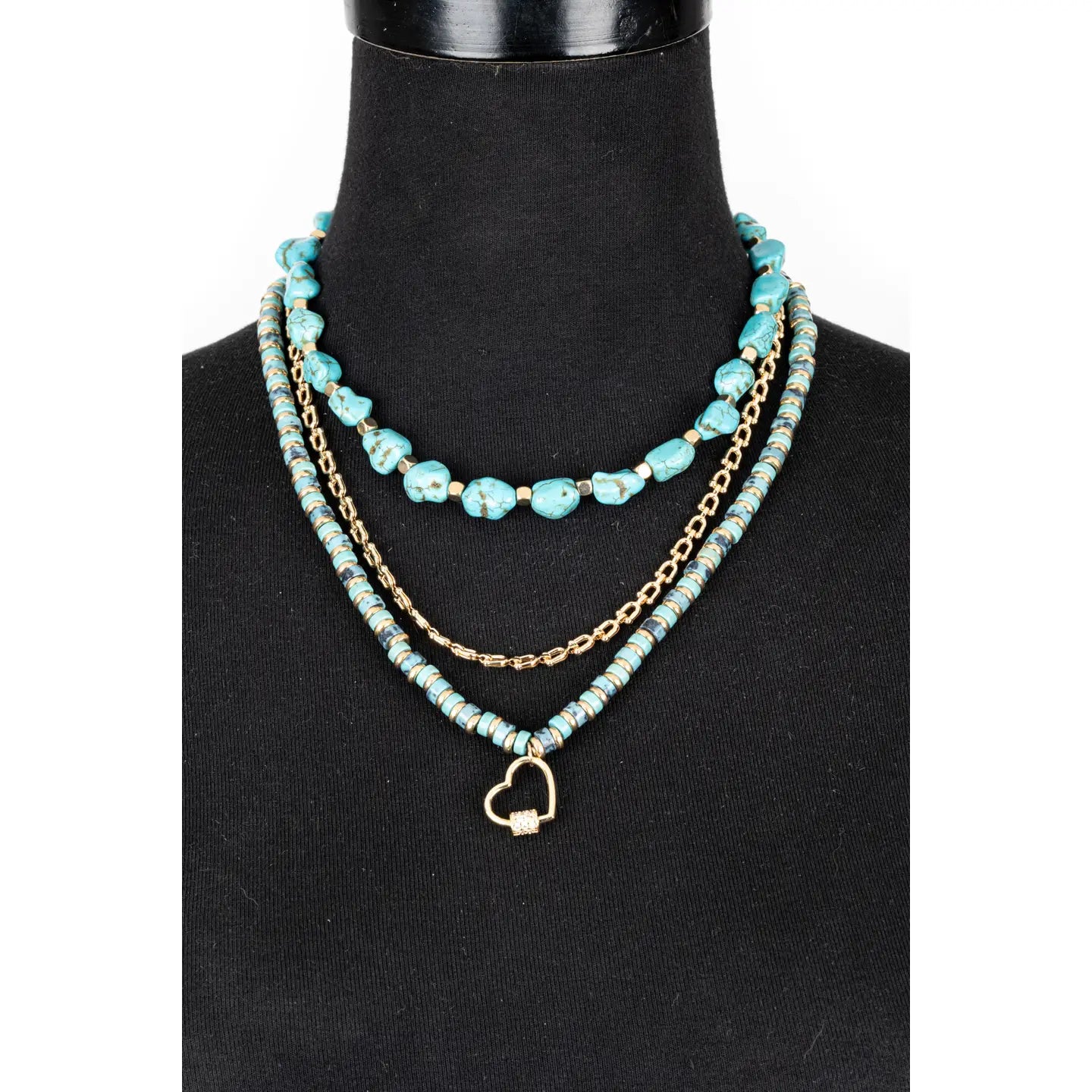 Layered turquoise bead necklace with gold chain and small heart charm on white background.