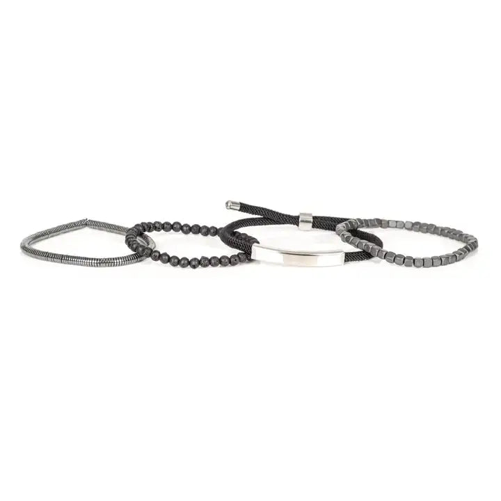 Men’s layered bracelet set featuring a polished silver-tone ID bar centerpiece, matte black lava stone beads, gunmetal cube beads, black braided cord wraps, and silver-tone coil wrap accents, stacked in a sleek industrial luxury design on a white background.