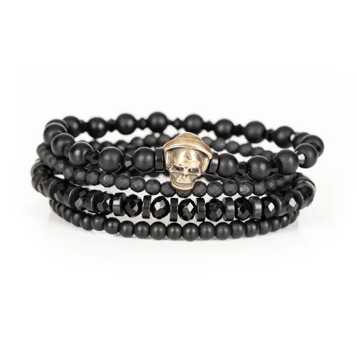 Black layered men’s bracelet set with matte black beads, gold skull centerpiece, faceted crystal accents, and geometric spacer beads on white background.