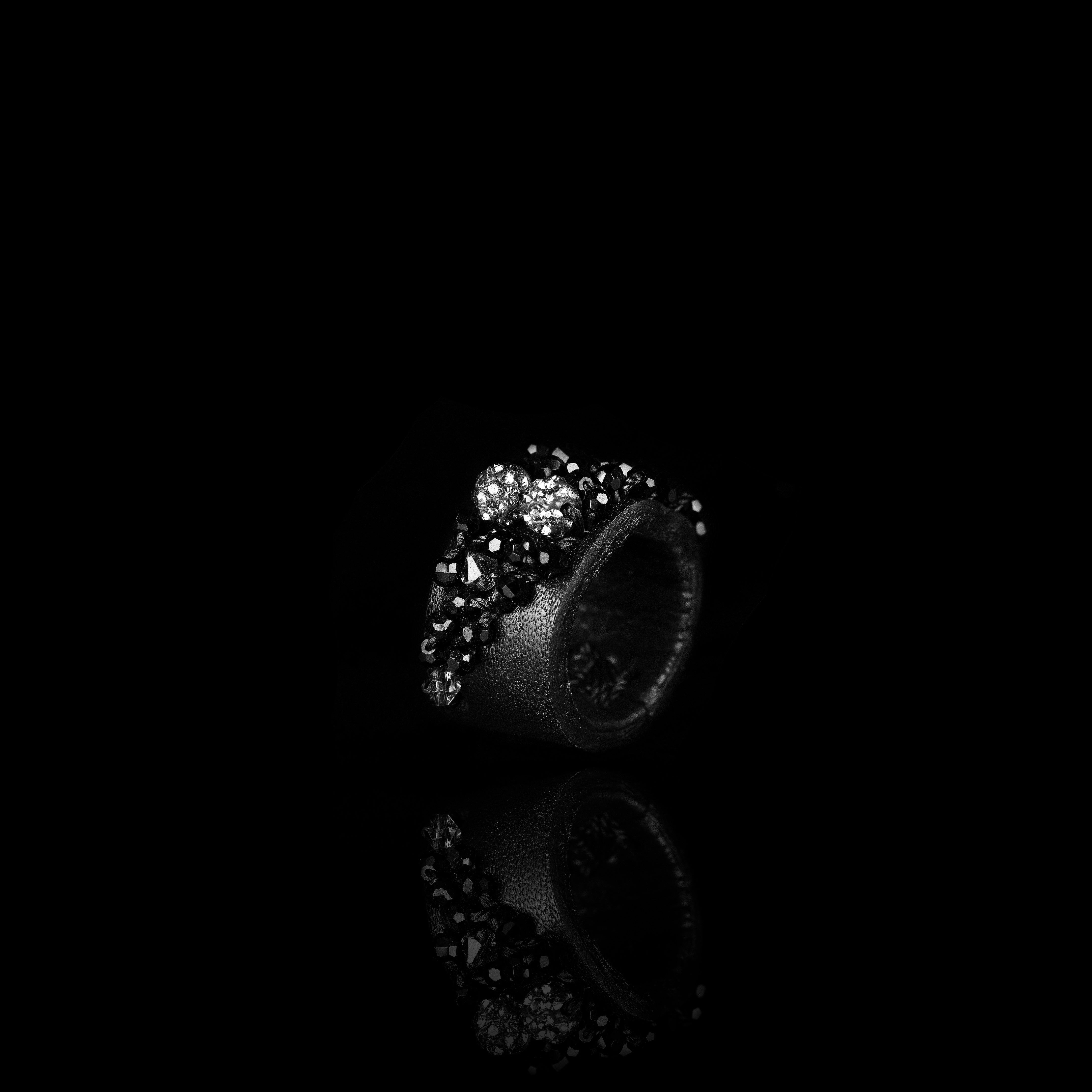 Handmade black leather statement ring with clustered black crystals and metallic pavé bead accents on white background